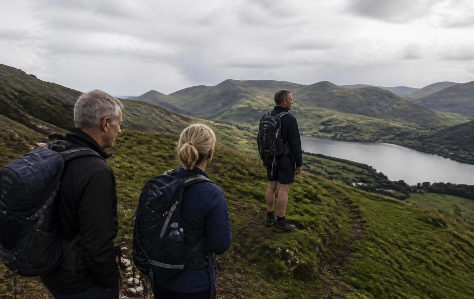 Walkers looking out over green hills and a lake in the UK